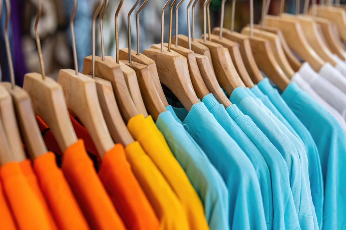 Colorful bright cotton T-Shirt with wooden hanger were hanging on the rack, for sale at modern apparel fashion store. Close-up with selective focus.